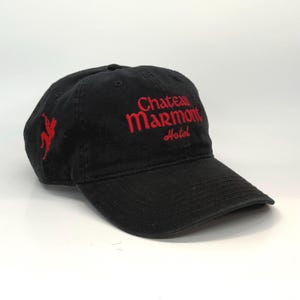 Puede incluir: Gorra de béisbol negra con texto bordado en rojo que dice "Chateau Marmont Hotel" y una figura bordada en rojo en el lateral.