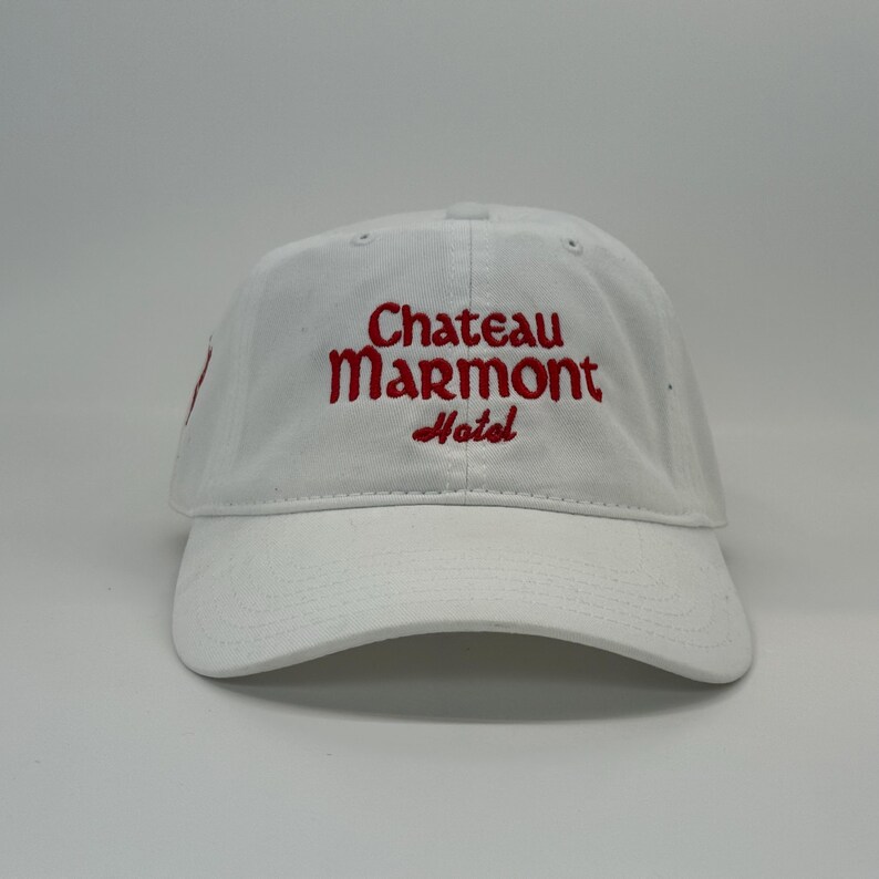 May include: White baseball cap with the embroidered text "Chateau Marmont Hotel" in red. The cap has a curved brim and a classic six-panel design, suitable for casual wear.