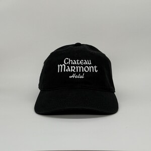 May include: Black baseball cap with the text "Chateau Marmont Hotel" embroidered in white. The cap has a curved brim and a classic six-panel design. A stylish accessory for casual wear.