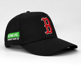 May include: Black baseball cap with a red and white embroidered "B" logo. The cap has a curved peak and a green patch with the text "KENMORE FENWAY PARK". A classic sports accessory.