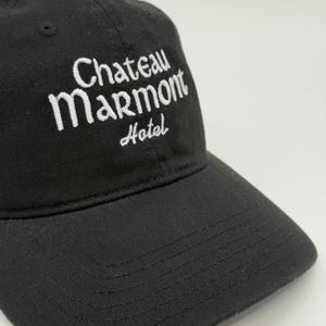 May include: Black baseball cap with the embroidered text "Chateau Marmont Hotel" in white. The cap has a curved brim and a small, black button on top. The hat is made of a soft, durable fabric.