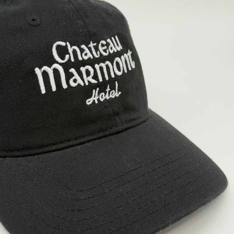 May include: Black baseball cap with the embroidered text "Chateau Marmont Hotel" in white. The cap has a curved brim and a small, black button on top. The hat is made of a soft, durable fabric.