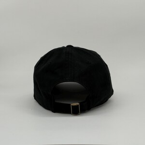 May include: Black baseball cap with a curved brim and adjustable metal buckle closure. The cap is made of a solid black fabric and features a rounded crown. The back of the cap has a metal buckle for size adjustment.