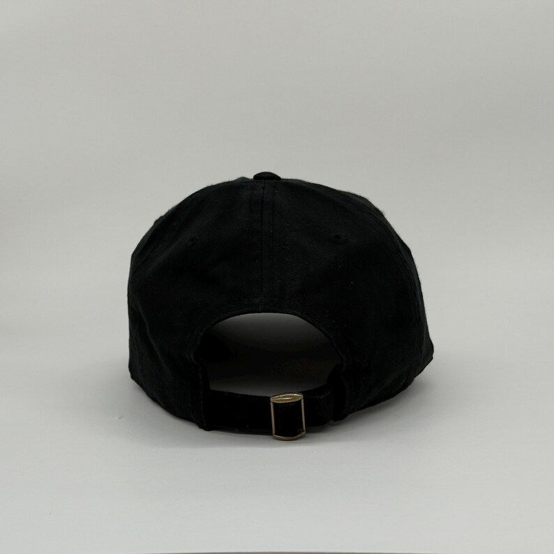 May include: Black baseball cap with a curved brim and adjustable metal buckle closure. The cap is made of a solid black fabric and features a rounded crown. The back of the cap has a metal buckle for size adjustment.