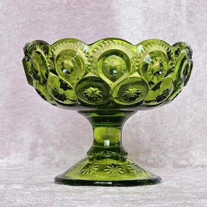 May include: A green glass candy dish with a pedestal base. The dish has a scalloped edge and is decorated with a repeating pattern of raised circles and stars.