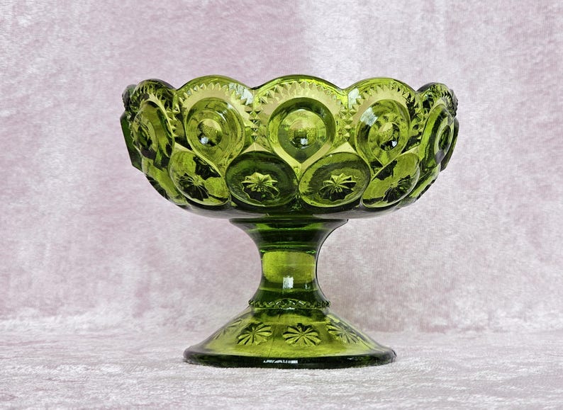 May include: A green glass candy dish with a pedestal base. The dish has a scalloped edge and is decorated with a repeating pattern of raised circles and stars.