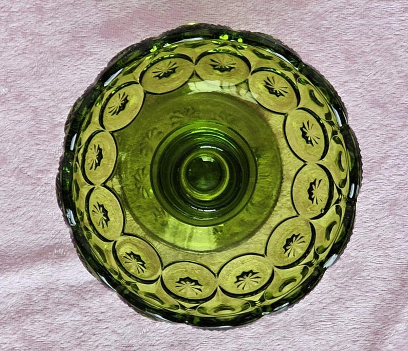 May include: A green glass pedestal bowl with a scalloped edge and a repeating pattern of stars. The bowl has a raised center base.