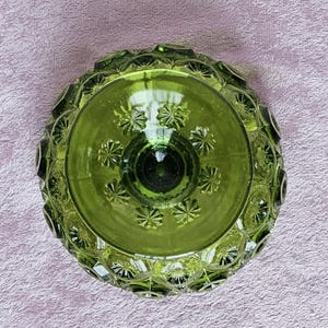 May include: A green glass bowl with a textured, raised pattern. The bowl has a round shape and a wide, shallow base.