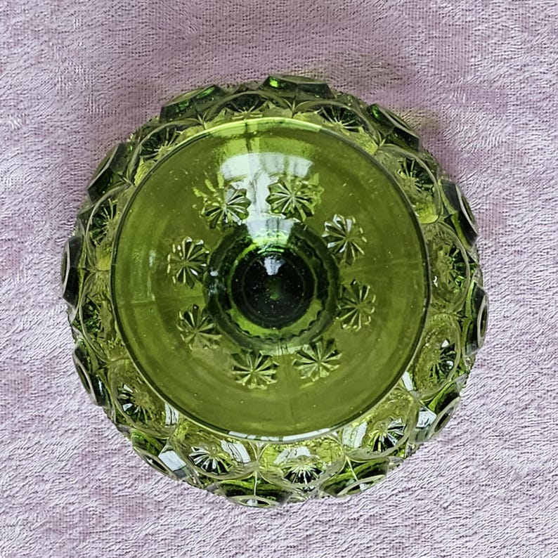 May include: A green glass bowl with a textured, raised pattern. The bowl has a round shape and a wide, shallow base.