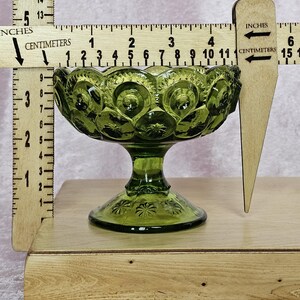 May include: A green glass candy dish with a pedestal base. The dish has a scalloped edge and a pattern of small circles and stars. The dish is approximately 3 inches tall and 5 inches wide.