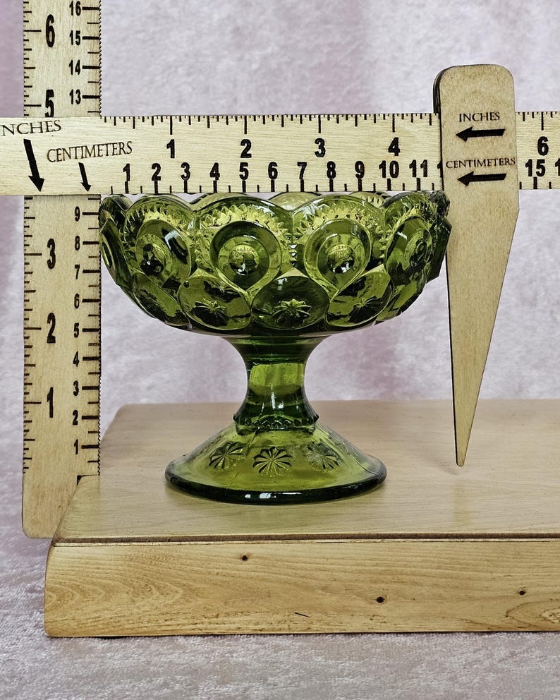May include: A green glass candy dish with a pedestal base. The dish has a scalloped edge and a pattern of small circles and stars. The dish is approximately 3 inches tall and 5 inches wide.