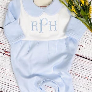 May include: A light blue baby romper with a white bib-style front. The romper features a Peter Pan collar and long sleeves. The white bib has the embroidered letters "RPH" in light blue. The tag reads "The Blue Vine Boutique".