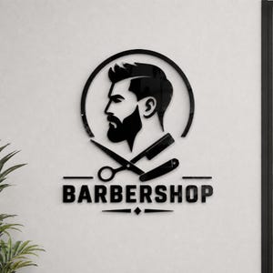 Könnte beinhalten: Schwarzes Friseursalon-Logo mit dem Profil eines Mannes in einem Kreis, mit Bart und stilvollem Haarschnitt. Darunter werden gekreuzte Schere und ein Rasiermesser angezeigt, darunter das Wort "BARBERSHOP".
