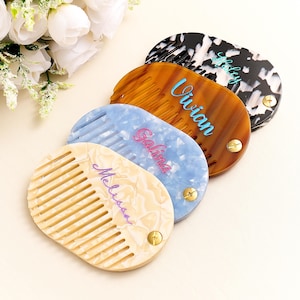 May include: A selection of personalised combs in shades of cream, blue, and tortoiseshell. Each comb displays a name in a contrasting colour, like "Melissa," "Galina," and "Vivian." The combs are oval and fastened with a brass-coloured rivet.