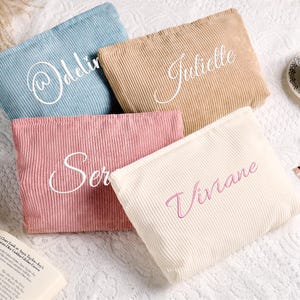 Op de afbeelding: Vier rechthoekige corduroy etuis in lichtblauw, beige, oudroze en crème. Elk etui is voorzien van een naam geborduurd in een cursief lettertype: Odelia, Juliette, Seraphina en Viviane. De etuis hebben een textuur van geribbelde stof.