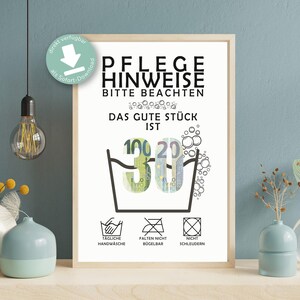 May include: A framed print with German text about laundry care instructions. The print features a graphic of a washing basin with money inside, along with icons for hand washing, no ironing, and no spinning. The text includes "PFLEGE HINWEISE" and "DAS GUTE STÜCK IST".