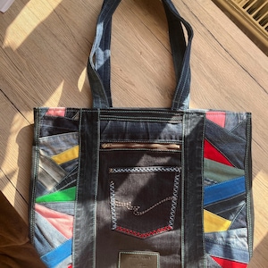 Könnte beinhalten: Jeans-Tote-Tasche mit farbigen Patchwork-Akzenten in Rot, Blau, Gelb und Grün. Die Tasche hat eine Fronttasche mit Reißverschluss und ein Etikett mit der Aufschrift "JACK & JONES". Sie hat zwei Jeans-Tragegriffe.