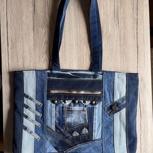 Könnte beinhalten: Eine Patchwork-Jeans-Tragetasche mit verschiedenen Blautönen. Die Tasche hat eine Reißverschlusstasche, dekorative Nieten und ein Knopfdetail. Die Griffe sind einfarbig dunkelblau.