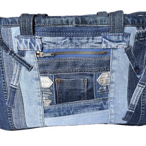 Könnte beinhalten: Eine rechteckige Tragetasche aus verschiedenen blauen Denim-Stoffflicken. Die Tasche verfügt über eine horizontale Reißverschlusstasche, eine kleine offene Tasche, zwei Tragegriffe und dekorative Denim-Streifen, die auf der Vorderseite aufgenäht sind.