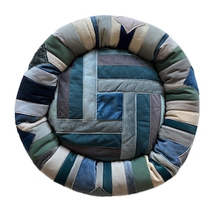 Könnte beinhalten: Ein rundes Haustierbett mit einem Patchwork-Design aus rechteckigen Stoffstreifen in verschiedenen Blau-, Grün-, Grau- und Beigetönen. Das mittlere Kissen ist von einem dicken, gepolsterten Rand umgeben, der aus zusammengenähten Stoffstücken besteht.