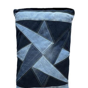 Könnte beinhalten: Ein rechteckiges Dekokissen aus wiederverwertetem Jeansstoff. Die Vorderseite zeigt ein geometrisches Sternmuster, das durch abwechselnde Bahnen aus dunkelblauem und hellblauem Denim entsteht, die mit sichtbaren Steppnähten verbunden sind.