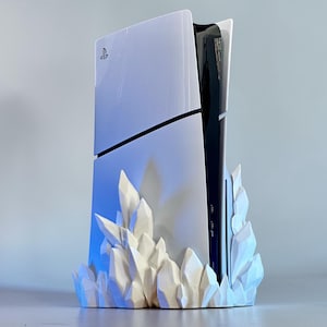 May include: A white and black gaming console with a stylized white crystal base. The console has a sleek design with the PlayStation logo visible. The crystal base adds a unique, artistic touch to the gaming setup.
