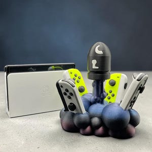 Könnte beinhalten: Eine weiße Nintendo Switch-Konsole und Controller werden mit einem speziell angefertigten Ständer präsentiert. Der Ständer hat die Form einer stilisierten Wolke mit einer Rakete, und die Controller sind weiß und neongrün.