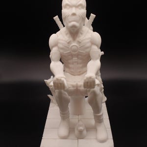 May include: White 3D printed figurine of a superhero character sitting on a throne. The character is wearing a mask and has a muscular build. The throne is decorated with swords and other details.