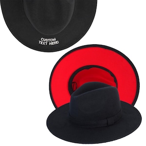 May include: A black fedora hat with a red interior. The hat has a black band and a white embroidered inscription that reads "CUSTOM TEXT HERE!"