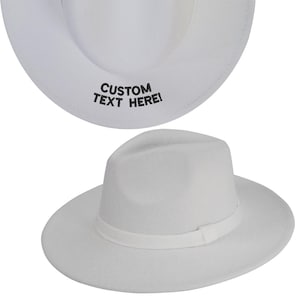 May include: A white fedora hat with a white band around the crown. The hat has the text "CUSTOM TEXT HERE!" embroidered on the inside of the brim.