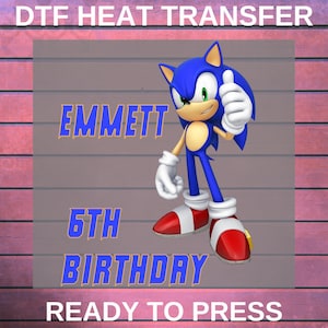 May include: A DTF heat transfer design featuring the character Sonic the Hedgehog giving a thumbs up. The design includes the name "EMMETT", "5TH BIRTHDAY", and the text "READY TO PRESS" in blue. The background has a wood-like texture.