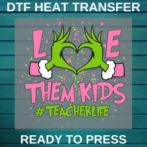 May include: A DTF heat transfer design with the words "LOVE THEM KIDS" in pink, featuring green hands forming a heart. The design includes the hashtag "#TEACHERLIFE" in green and is ready to press.