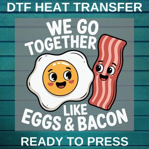May include: DTF heat transfer design featuring a cartoon egg and bacon with smiling faces. The text reads "WE GO TOGETHER LIKE EGGS & BACON READY TO PRESS". The design is on a transparent background.