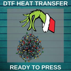 May include: A DTF heat transfer design featuring a green hand holding a tangled ball of Christmas lights. The hand is wearing a white cuff with a red sleeve. The text "READY TO PRESS" is at the bottom.