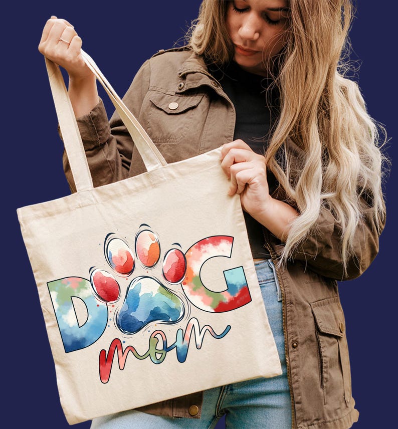 May include: A white canvas tote bag with a colorful watercolor design of a paw print and the words "Dog Mom".