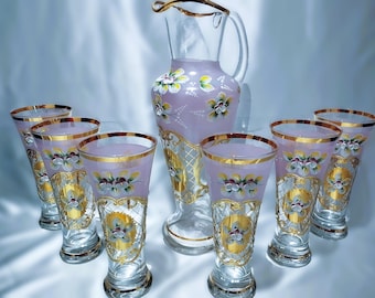 May include: A decorative glass drinkware set featuring a pitcher and eight matching glasses. The set has a light purple hue with gold trim and floral designs. The glasses are approximately 6 inches tall.