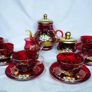 May include: A ruby red tea set with gold accents. The set includes a teapot, sugar bowl, and several teacups with matching saucers. Floral and lattice designs adorn the set, creating an elegant aesthetic.