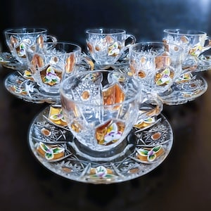 May include: A set of six clear crystal teacups and saucers. Each cup and saucer features a floral design with gold and orange accents. The crystal is cut with a starburst pattern.