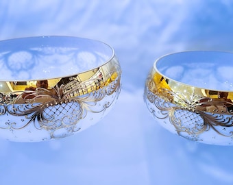 May include: Two white bowls with gold trim and intricate designs. The bowls are different sizes and are on a blue background.