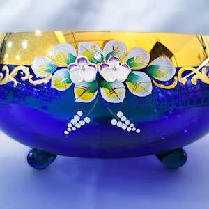 Cuenco de vidrio azul bohemio con decoración floral esmaltada en oro y tres patas.