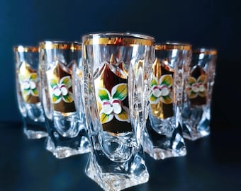 May include: Set of six clear glass shot glasses with gold rims and floral designs. Each glass features a different floral design with white, yellow, and green accents.