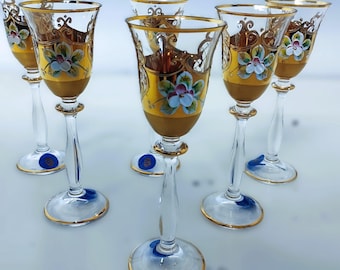 May include: Set of six clear glass shot glasses with gold trim and painted floral designs. The glasses have a delicate, elegant design.