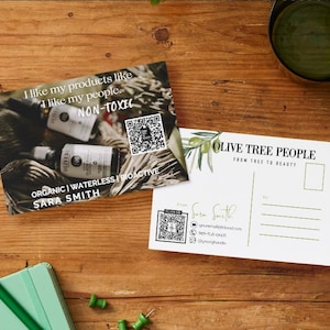 May include: Two postcards and a small notebook on a wooden surface. One postcard features a product image with text: "I like my products like I like my people. NON-TOXIC. ORGANIC | WATERLESS | BIOACTIVE SARA SMITH." The other postcard says "OLIVE TREE PEOPLE FROM TREE TO BEAUTY."