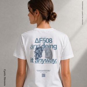 Könnte beinhalten: Weißes T-Shirt mit einem Grafikdesign auf dem Rücken. Das Design enthält den Text "ΔF508 and doing it anyway." und eine blaue Blumenillustration neben einer Lungenillustration. Die Worte "Cystic fibrosis" sind vertikal auf der linken Seite gedruckt.