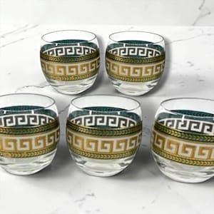 May include: A set of five clear glass tumblers, each featuring a decorative band around the middle. The band consists of a gold-coloured Greek key pattern bordered by a dark teal and gold leaf-like design on the top and bottom edges.
