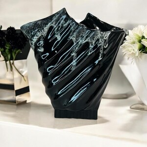 May include: A black ceramic vase with a unique, angular design. The vase has a glossy finish with white and light blue accents. The vase has a textured, swirling pattern and is suitable for displaying flowers. The vase is approximately 10 inches tall.