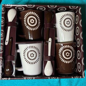 May include: Set of four brown and white mugs with a geometric pattern and four matching spoons in a brown box with a white and brown patterned design.