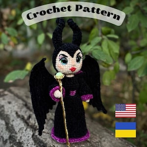 Puede incluir: Muñeca de ganchillo de un personaje con cuernos negros, alas y un vestido negro con ribetes morados. La muñeca sostiene un bastón dorado con un orbe verde. El texto "Crochet Pattern" está encima de la muñeca. Las banderas estadounidense y ucraniana están en la imagen.