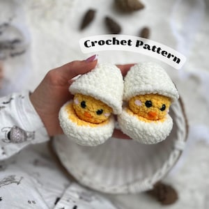 May include: Two crocheted chicks in eggshells. The chicks are yellow with black eyes and beaks. The eggshells are white and crocheted.