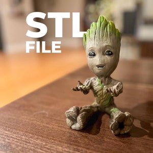 May include: A 3D-printed figure of the character Groot from Guardians of the Galaxy. The figure is sitting with its arms outstretched. The text "STL FILE" is displayed in white letters above the figure.